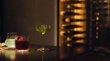 Drei bunte Cocktails auf einem dimmen Tresen.