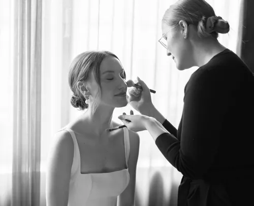 Woman applying makeup to seated person indoors.