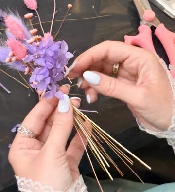 Hände arrangieren Blumen auf dunkler Fläche.