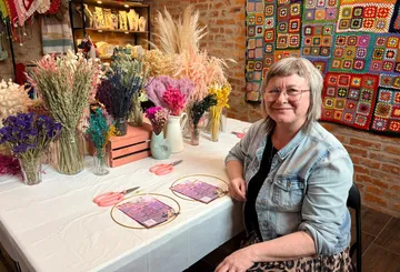 Frau sitzt am Tisch mit Blumenarrangement.