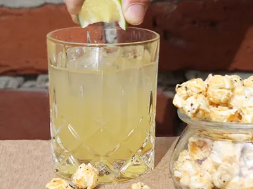 Glass with drink is garnished with lime; popcorn next to it.