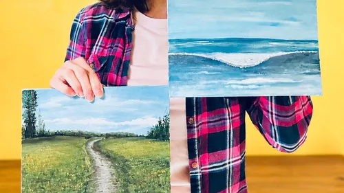 Person holding two landscape paintings indoors.