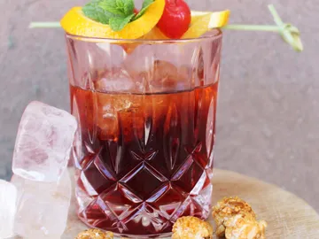 Glass with drink, ice cubes and snacks next to it.
