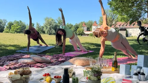 Drei Frauen machen Yoga auf Gras mit Picknick.