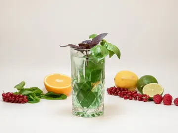A glass with a cocktail and fresh fruit next to it.