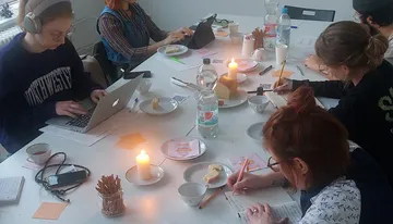People writing, studying around candlelit table.