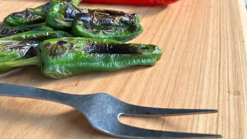 Gegrillte grüne Paprika auf einem Holzbrett.