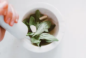 Basil leaves in mortar being crushed.