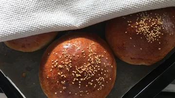 Drei Brötchen mit Sesam unter einem Tuch.