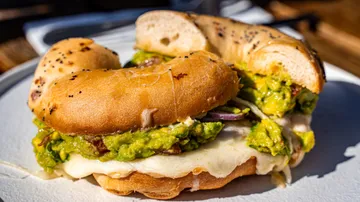 Bagel mit Guacamole und Käse auf Teller.