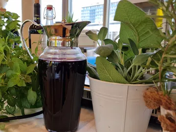 Carafe with dark drink next to fresh herbs, bright surroundings.