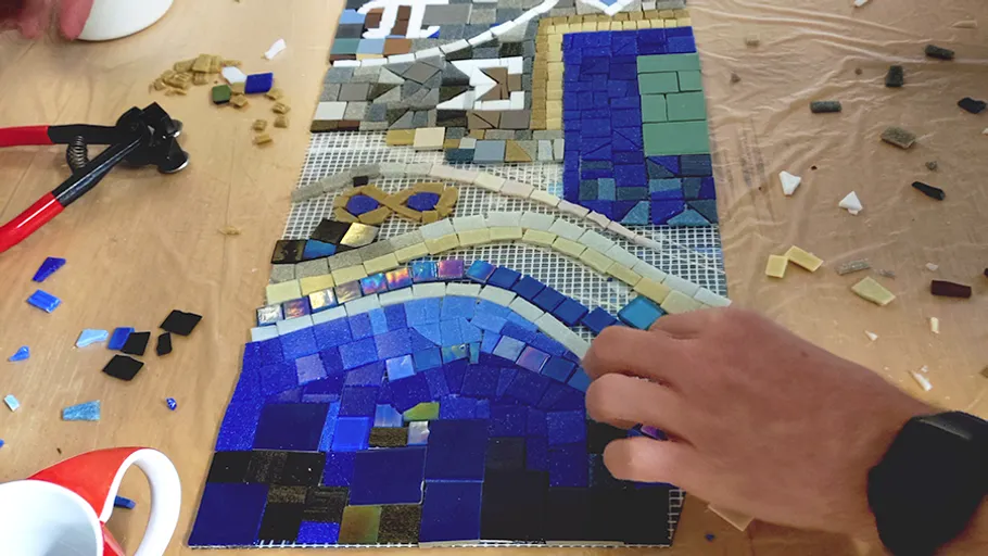 Hand legt Fliesen in einem Mosaikprojekt.
