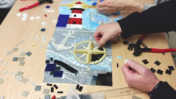 Hände bauen Mosaik auf Holztisch zusammen.