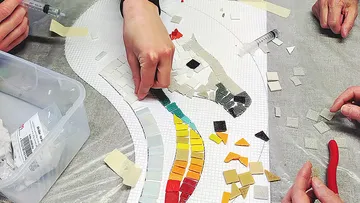 Hände gestalten ein buntes Mosaikpferd.