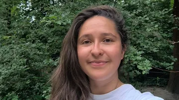 Person smiling in lush green forest.