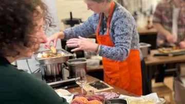 Person cooking in kitchen with others watching.