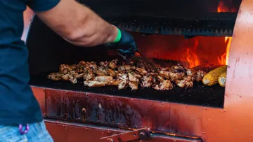 Person grillt Hühnchen und Mais auf Grill.