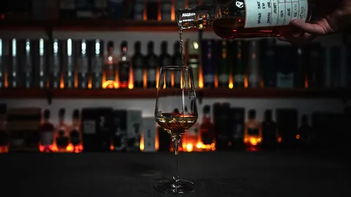 Bottle pouring whiskey into glass, bar background.