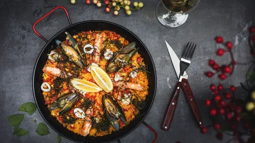 Meeresfrüchte-Paella in einer Pfanne auf dunklem Tisch.