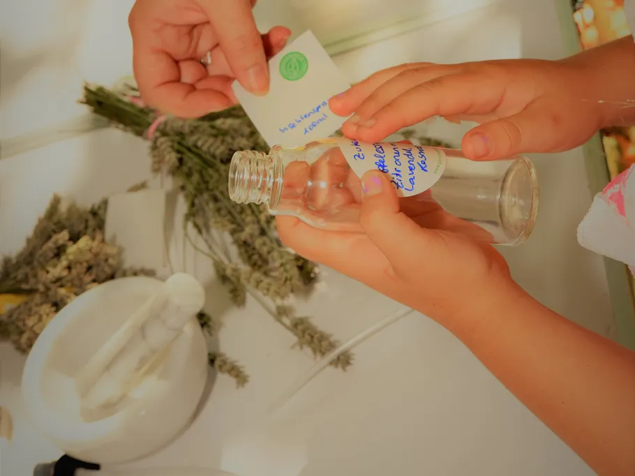 Hände, die eine Glasflasche etikettieren, getrocknete Kräuter in der Nähe.