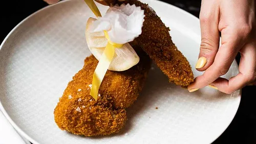 Hands placing breaded meat on plate.