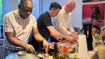 Drei Männer bereiten Essen in Küche vor.