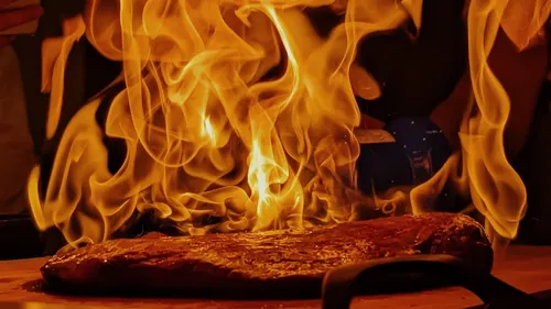 Grilled steak engulfed in flames, kitchen setting.