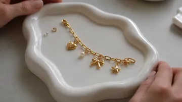 Goldenes Armband mit Anhängern auf Keramiktablett.