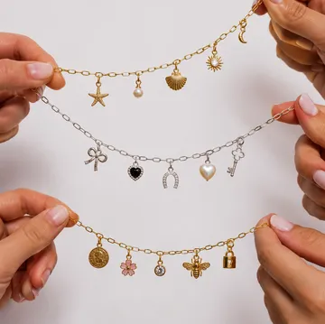 Hände halten Armbänder mit Anhängern in neutraler Umgebung.