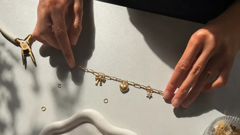 Hände fertigen goldenen Charm-Armband.