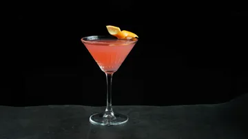 Rosafarbener Cocktail mit Orangengarnitur, schwarzer Hintergrund.