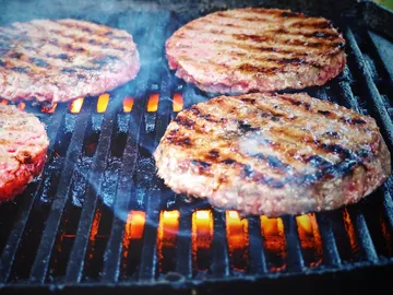 Grilled burger patties sizzle over an open fire.