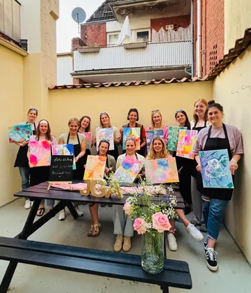 Gruppe von Frauen zeigt bunte Gemälde im Freien.