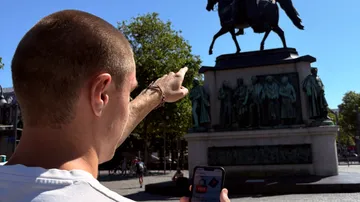 Person pointing at horse statue, holding smartphone.