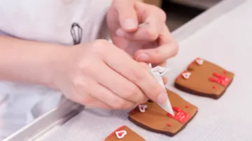 Hände dekorieren Kekse mit Zuckerguss auf Tisch.
