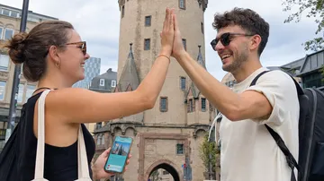 Two people high-five outdoors by a tower.