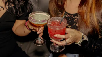 Zwei Frauen halten Cocktails an der Bar.