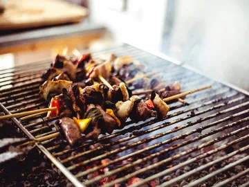 Roast barbecue skewers over glowing coals in a kitchen.