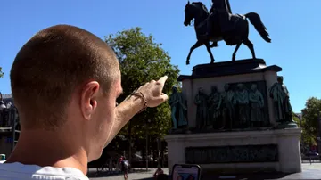 Person zeigt auf Reiterstatue im Freien.