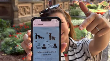 Frau zeigt draußen Smartphone mit Quiz-App.