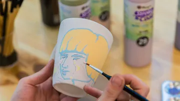 Person painting face on ceramic cup.