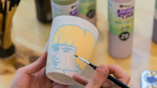 Person painting face on ceramic cup.