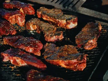 Roast pieces of beef on a grill in a sunny environment.