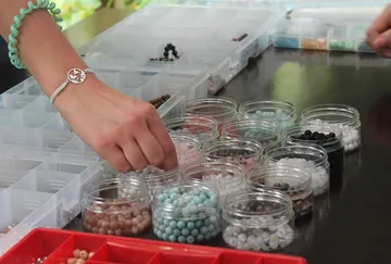 Hands sorting beads into small containers.