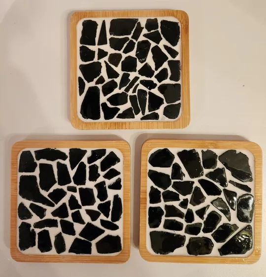 Drei quadratische Untersetzer mit schwarzem Mosaikmuster.