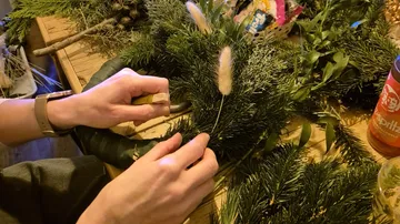 Hände arrangieren Weihnachtskranz auf Tisch.