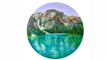 Berg spiegelt sich in einem See, umgeben von Bäumen.