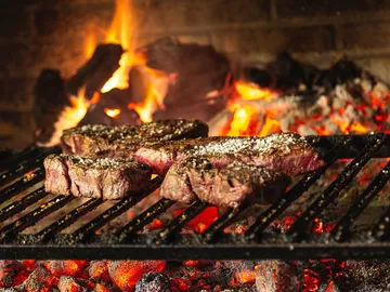 Steaks braten über glühender Kohle in einem offenen Grill.
