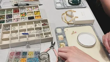 Hände basteln Schmuck mit Perlen auf Tisch.
