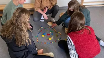Fünf Personen sitzen und legen bunte Steine drinnen.